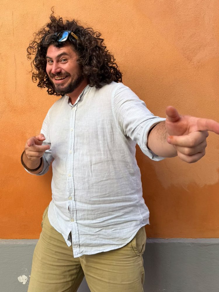 Fabio Antichi davanti a un muro arancio, sorridente, indica chi guarda